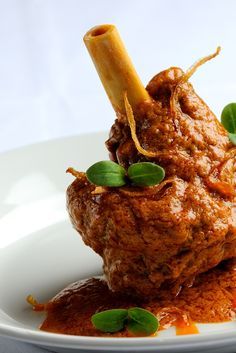 a white plate topped with meat covered in sauce and garnished with green leaves