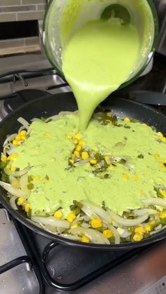 someone is pouring green sauce into a skillet on top of the stove with vegetables in it