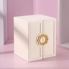 a small white box with a gold ring on it's front and inside, against a pink background