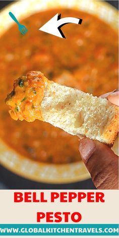 a hand holding a piece of bread over a bowl of soup with the words bell pepper pesto on it