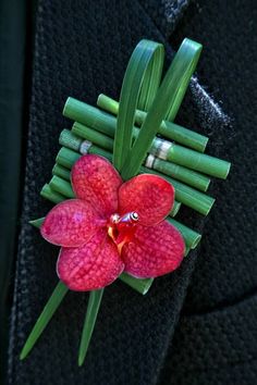 a red flower with green stems attached to the lapel of a black suit jacket