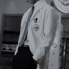 a man wearing a white lab coat and tie standing in front of a machine room