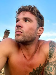 a shirtless man with tattoos on his chest looking up at something in the sky