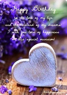 a wooden heart sitting on top of a table next to purple flowers