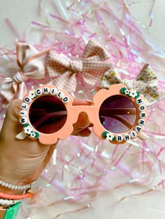 a person holding up some pink sunglasses with words on them and bows in the background