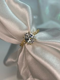 a diamond ring on top of a white satin fabric with a bow in the middle