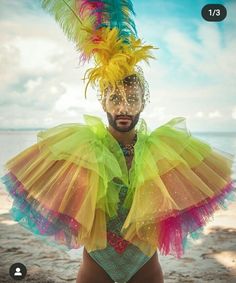 a man wearing a colorful costume and headpiece with feathers on his head standing in front of the ocean