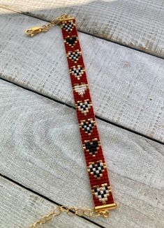 a red and black beaded bracelet on a wooden surface with gold chains hanging from it