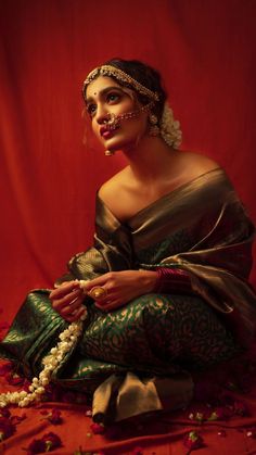 a woman in a green and gold sari sits on the floor with beads around her neck