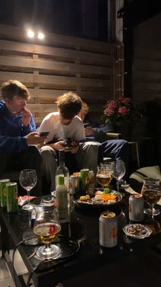 three people sitting around a table with food and drinks on it, looking at their cell phones