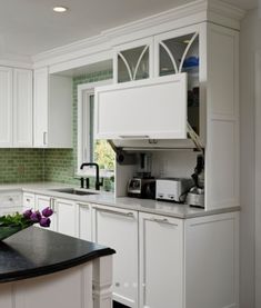 a kitchen with white cabinets and green tile backsplash, black countertops and an island