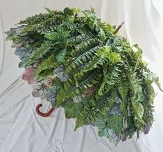 an umbrella made out of plants and leaves on a white cloth covered surface with a wooden handle