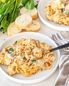 two white plates filled with pasta and spinach on top of a table next to bread