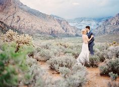 a bride and groom standing in the desert with mountains in the background at their wedding