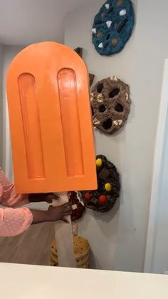 a person holding an orange object in front of a wall with donuts on it