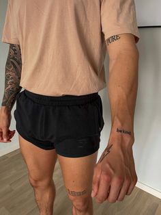 a man with tattoos on his arm and leg standing in front of a white wall