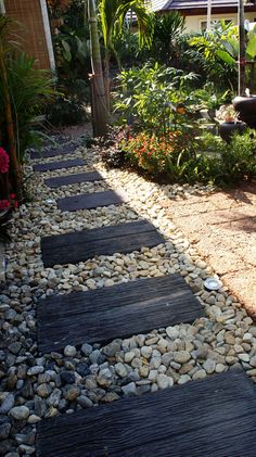 a walkway made out of wood and rocks in the middle of a garden with flowers