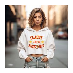 "Classy Until Kickoff Crop Hoodie, SBLVIII Sweatshirt, Cute Football Sweatshirt for big game, Swiftie Fan Football Hoodie, Kelce Bowl Game 💖 WELCOME TO MY STORE, I'M SO HAPPY YOU STOPPED BY💖 My main aim is to ensure your happiness and satisfaction. I truly value your patronage. If you have any questions or would like a custom-made design, please don't hesitate to reach out. Even if you love the design but aren't fond of the available sweatshirt colors, feel free to contact me. I'll go above and beyond to ensure your satisfaction.  To communicate with me regarding any inquiries, concerns, or customization requests, please use the \"Add message to seller\" link on the checkout page. Shirt Details: Lane Seven Cropped Hoodie *85% combed ringspun cotton, 15% polyester *Medium fabric  *Relaxed White Hoodie For Sports Events In Fall, White Hooded Fan Apparel Top, White Cotton Hoodie For Game Day, Varsity Hoodie For Game Day In Fall, Sports Fan Long Sleeve Hoodie For Fall, White Sports Fan Hoodie For Winter, White Sports Fan Hoodie For Fan Gear, White Long Sleeve Hoodie For Football Season, Game Day Hooded Sweatshirt With Graphic Print