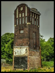 an old brick building sitting in the middle of a field next to trees and bushes