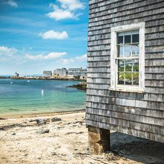 an old wooden building sitting on top of a sandy beach next to the ocean with boats in the water