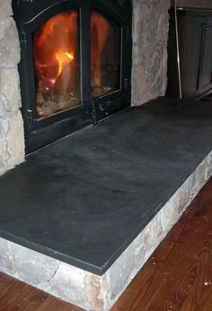 a fire place in the middle of a room with wood flooring and stone walls