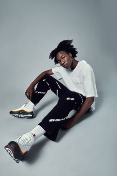 a man with dreadlocks sitting on the ground in front of a gray background