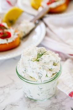 a small glass bowl filled with cream cheese and dill on top of a marble table