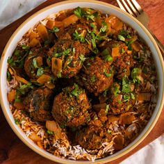 a white bowl filled with meatballs and rice on top of a wooden cutting board