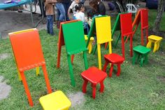 there are many different colored chairs in the grass with people looking at them from behind