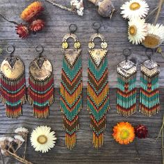 several pairs of beaded earrings are displayed on a wooden surface with flowers and dried grass