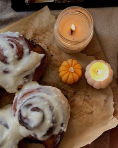 cinnamon rolls with white icing on top next to a candle and some pumpkins