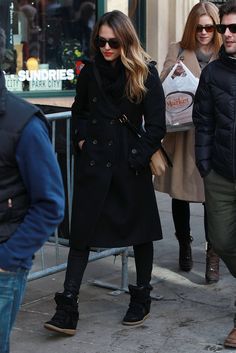 a woman in black coat and scarf walking down the street