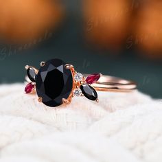 a black diamond ring with red and white stones on top of the band, sitting on a white blanket