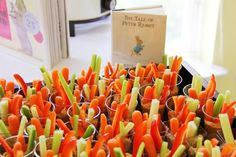 carrots and celery sticks are arranged in cups on a table next to a book