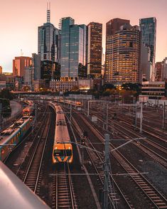 a train traveling down tracks in front of tall buildings at dusk with the sun going down