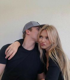 a young man and woman are hugging each other while posing for a photo in front of a white wall