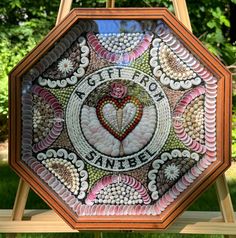 a wooden frame with an image of a heart and words painted on the inside, in front of some trees