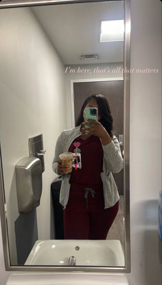 a woman taking a selfie in front of a mirror holding a drink and looking at her cell phone