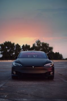 a black tesla car parked in a parking lot at sunset with trees in the background