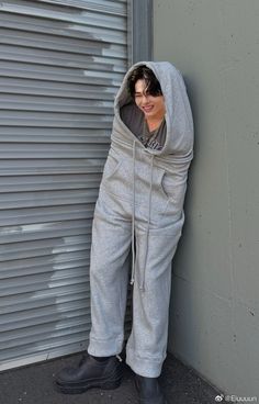 a young man leaning against a wall wearing a hoodie and sweatpants with his hands in the pockets