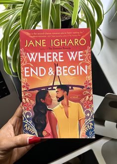 a person holding up a book about where we end and begin in front of a potted plant