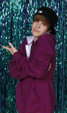 a boy in a purple jacket and black hat posing for a photo with green sequins behind him