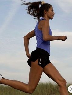 a woman is running in the grass with her hair blowing in the wind and she's wearing a blue tank top