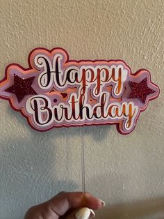 a hand holding a happy birthday sign on a stick in front of a white wall