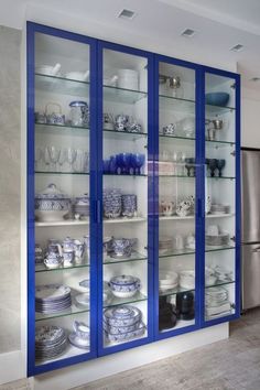 a blue and white china cabinet with glass shelves filled with plates, bowls and cups