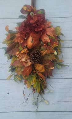 a wreath with autumn leaves and acorns hanging on a white wooden wall next to a pine cone