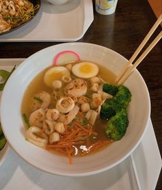 a bowl of soup with shrimp, broccoli and carrots on the side