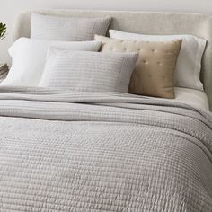 a bed with white sheets and pillows on top of it next to a potted plant