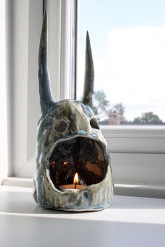 a ceramic animal head sitting on top of a window sill next to a lit candle