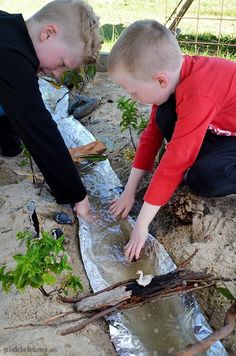 two children are playing in the sand with water and plants on it's side